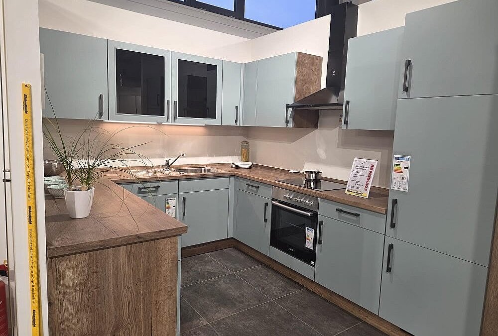 U-förmige Küche mit hellblauen Fronten, Holzarbeitsplatte und schwarzer Dunstabzugshaube – moderne Musterküche Touch bei KüchenMarkt Landshut Nord.