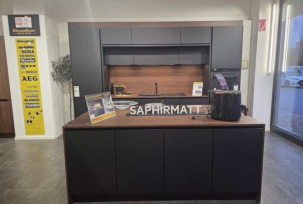 Gesamtansicht der Easytouch Musterküche (Koje 19) mit Insel und Zeile in Saphirmatt und Walnussholz-Akzenten.