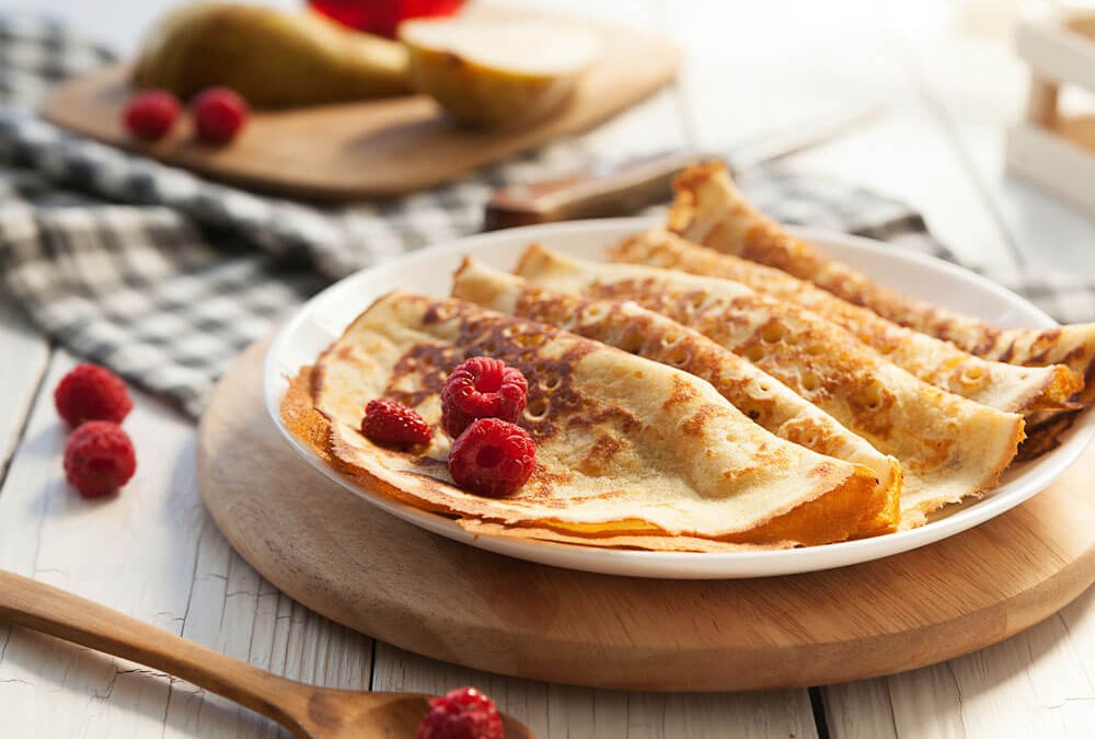 Perfekte, goldbraune Pfannkuchen mit frischen Himbeeren auf Teller – Ergebnis von richtig gegossenem Pfannkuchenteig
