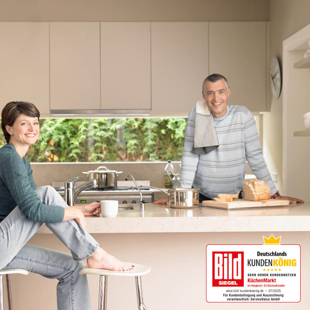 Glückliches-Paar in einer Küche mit Kücheninsel auf der Arbeitsfläche und das Siegel "Deutschlands-Kundenkönig".