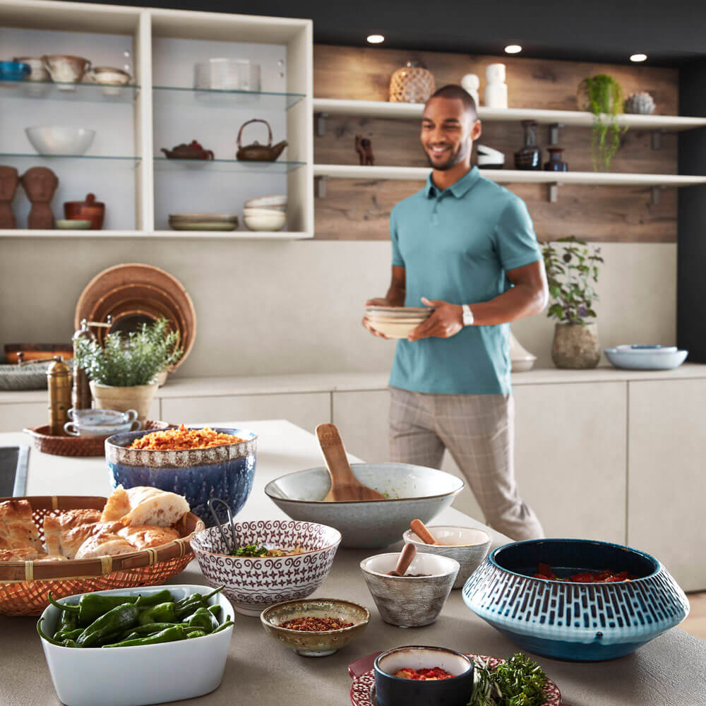 Effiziente Küchengestaltung: Mann in Küche mit vielfältigen, griffbereiten Küchenutensilien für angenehmes Kocherlebnis.