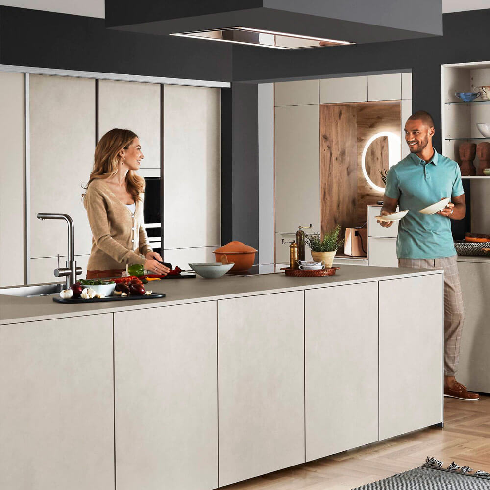 Rückenschonend Kochen: Paar in großer Küche mit Insel, ergonomische Platzierung der Arbeitsbereiche reduziert Belastung.