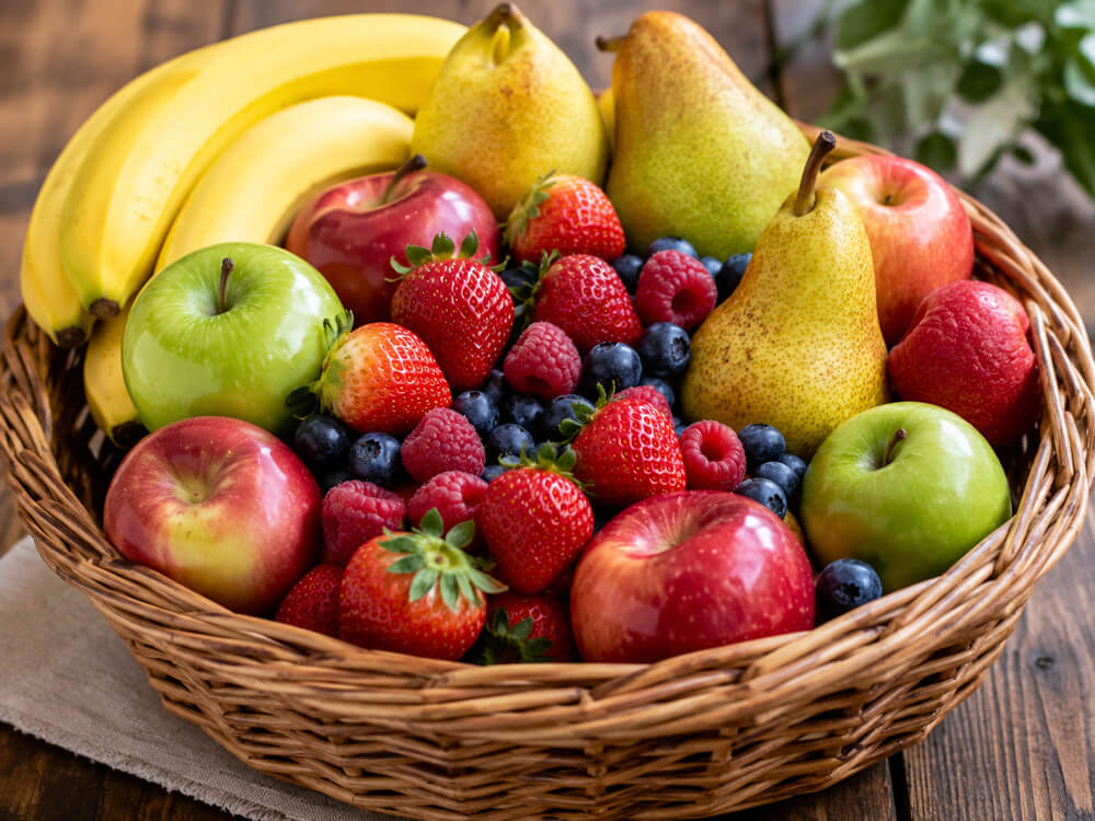 Bunter Obstkorb mit Beeren, Bananen, Äpfeln und weiterem frischem Obst