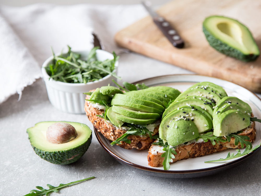 Knuspriger Avocado-Toast mit Rucola und Gewürzen auf einem weißen Teller