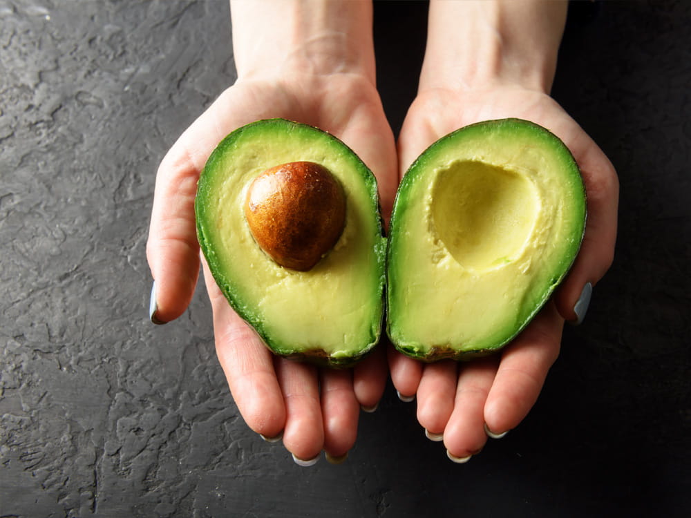 Zwei Hände präsentieren eine halbierte Avocado mit glattem braunem Kern