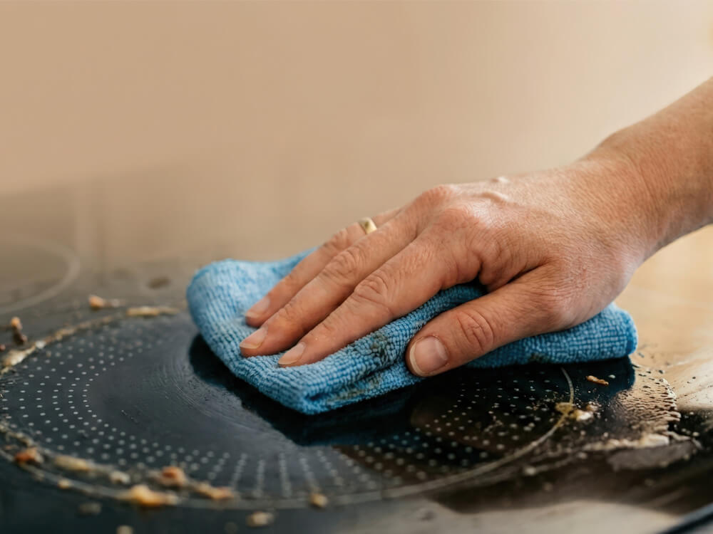Hand wischt Fettflecken von hellen Küchenfliesen mit einem Reinigungstuch ab