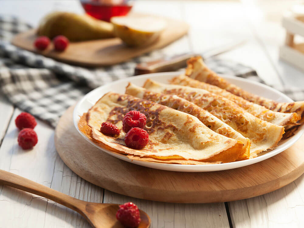 Perfekte, goldbraune Pfannkuchen mit frischen Himbeeren auf Teller – Ergebnis von richtig gegossenem Pfannkuchenteig