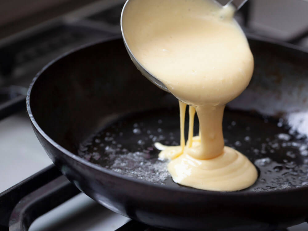 Pfannkuchenteig mit Schöpflöffel in heiße Pfanne gießen