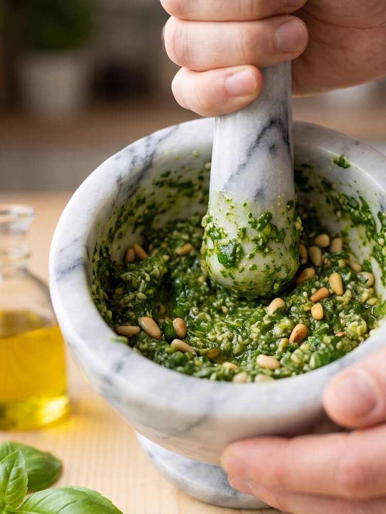 Basilikum wird im Mörser zu grünem Pesto verarbeitet