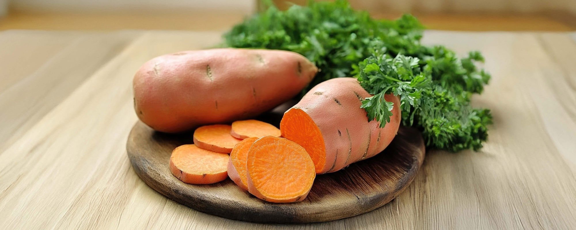 Rohe Süßkartoffeln geschnitten und ungeschnitten mit Petersilie auf Holzbrett in Küche