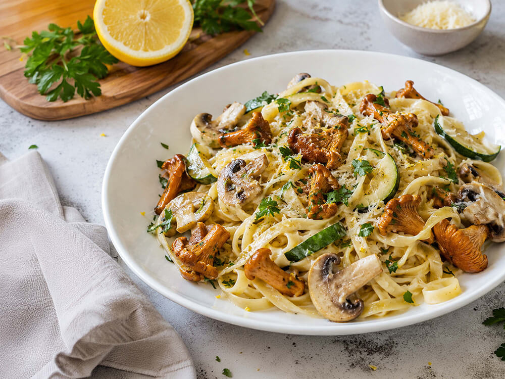 Pasta mit Pfifferlingen, Champignons, Zucchini und geriebenem Parmesan auf einem weißen Teller