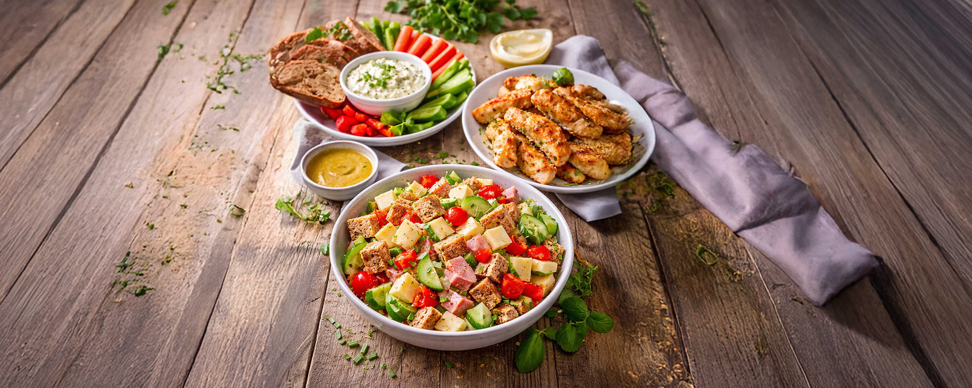 Variationen schneller Feierabendrezepte: Brotzeit-Bowl, Kräuterfrischkäse mit Rohkost und Hähnchenstreifen mit Dip auf einem Tisch.