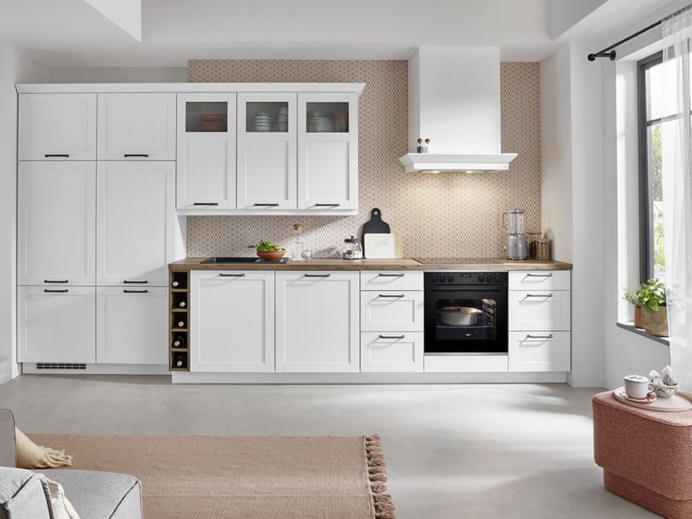 Helle Landhausküche in Weiß mit Bosch-Herd, dunklen Griffen und integriertem Flaschenregal aus Holz