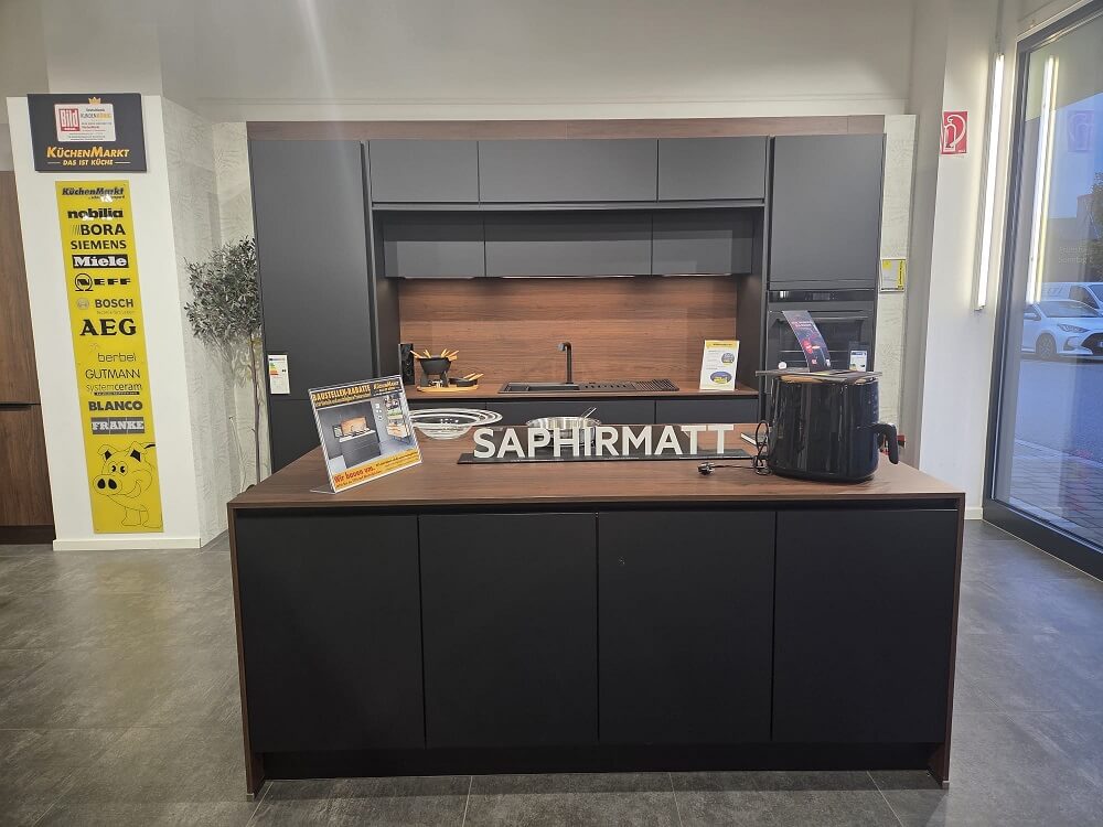 Gesamtansicht der Easytouch Musterküche (Koje 19) mit Insel und Zeile in Saphirmatt und Walnussholz-Akzenten.