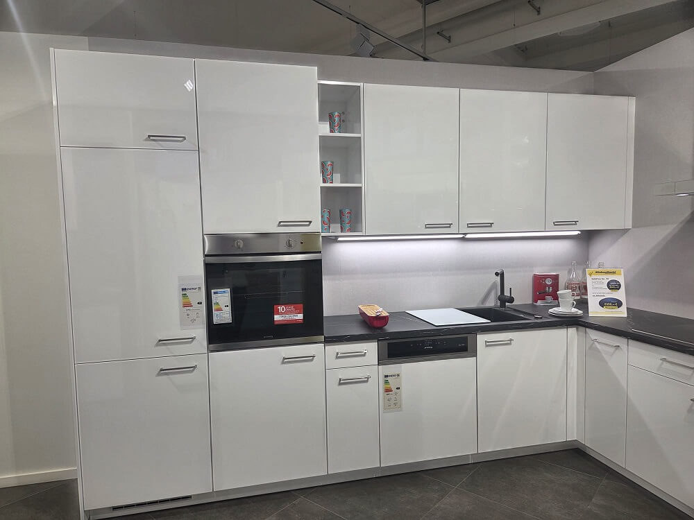 Hochschrank-Zeile der L-Küche Flash (Koje 32) in Alpinweiß Hochglanz, mit integriertem Backofen und Kühlschrank.