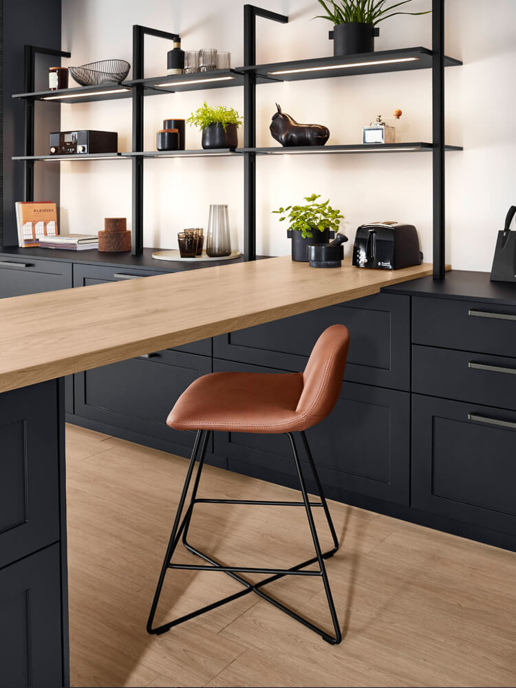 Küchen-Insel mit Holz-Arbeitsplatte und integriertem Bar-Sitzplatz neben einem schwarzen Regalsystem im modernen Nordic-Design